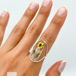 A silver ring with a clear oval-shaped setting containing a pressed yellow sunflower. The ring is designed with a curved adjustable band.