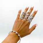 A silver bracelet with a twisted design. Three silver rings with openwork designs are worn on the fingers of a hand.