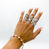 A silver bracelet with a twisted design. Three silver rings with openwork designs are worn on the fingers of a hand.