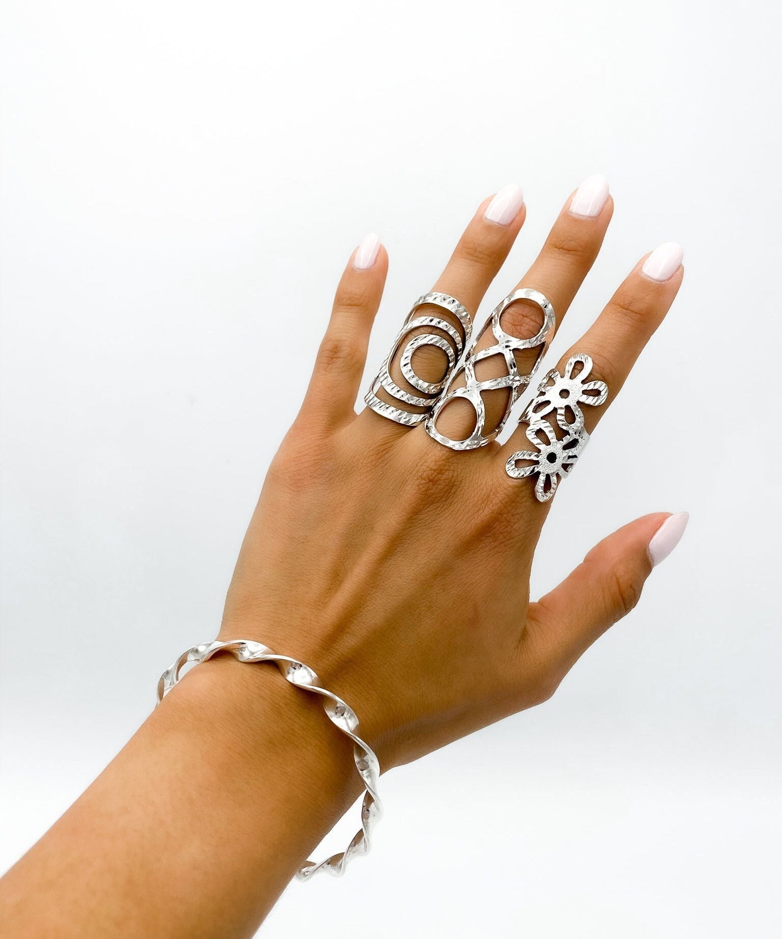 A silver bracelet with a twisted design. Three silver rings with openwork designs are worn on the fingers of a hand.