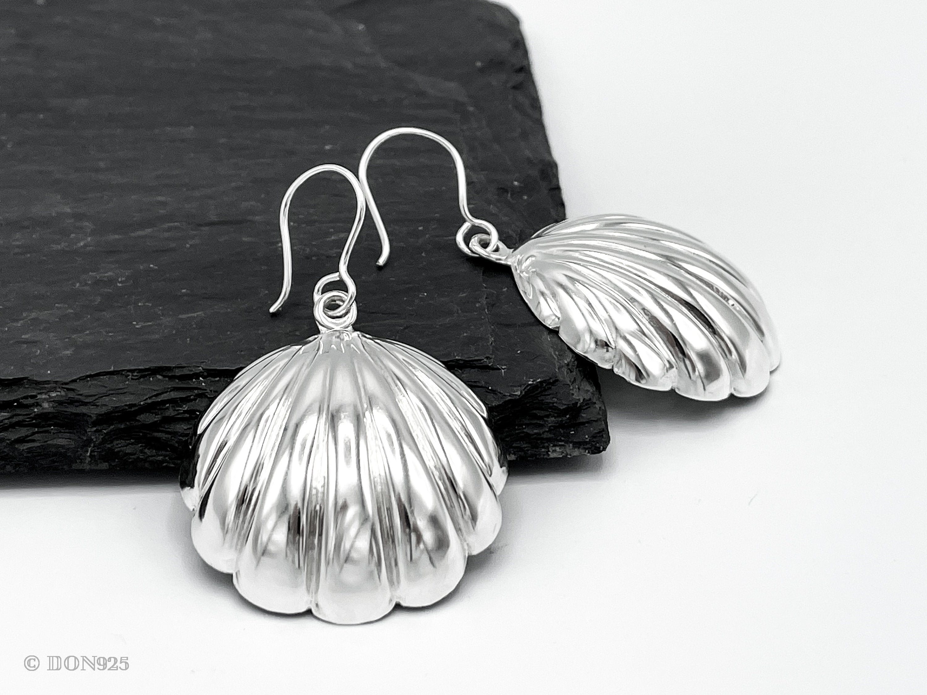 A pair of sterling silver seashell earrings with a hook.