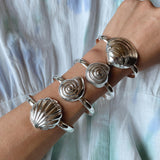 Sterling Silver seashell cuff bracelets on an arm, may include Clam shell, spiral shell, scallop shell.