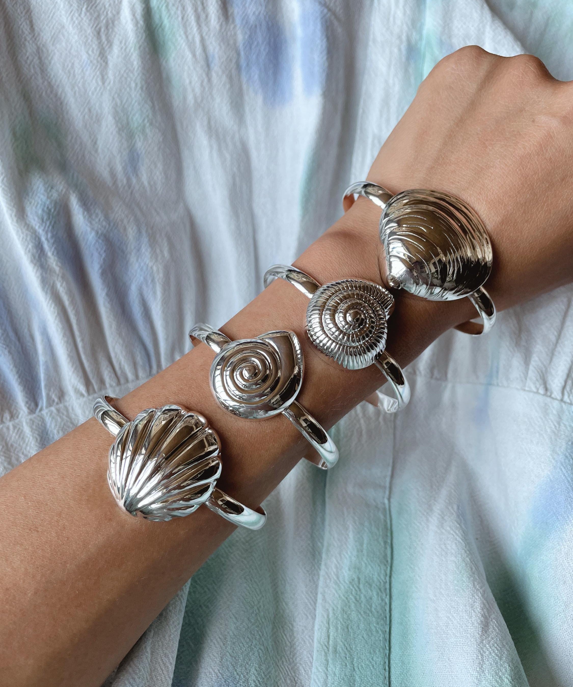 Sterling Silver seashell cuff bracelets on an arm, may include Clam shell, spiral shell, scallop shell.