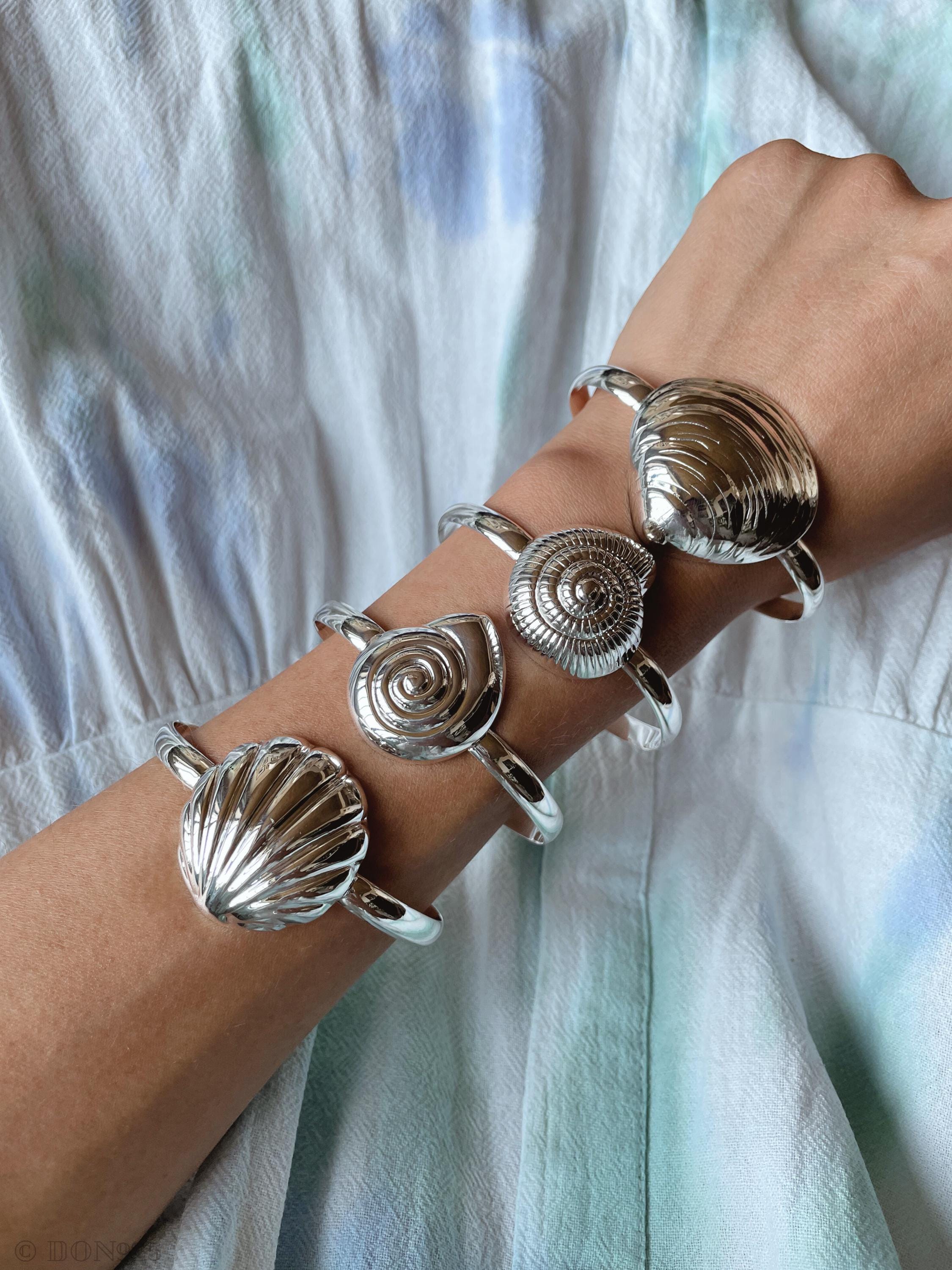 Sterling Silver seashell cuff bracelets on an arm, may include Clam shell, spiral shell, scallop shell.