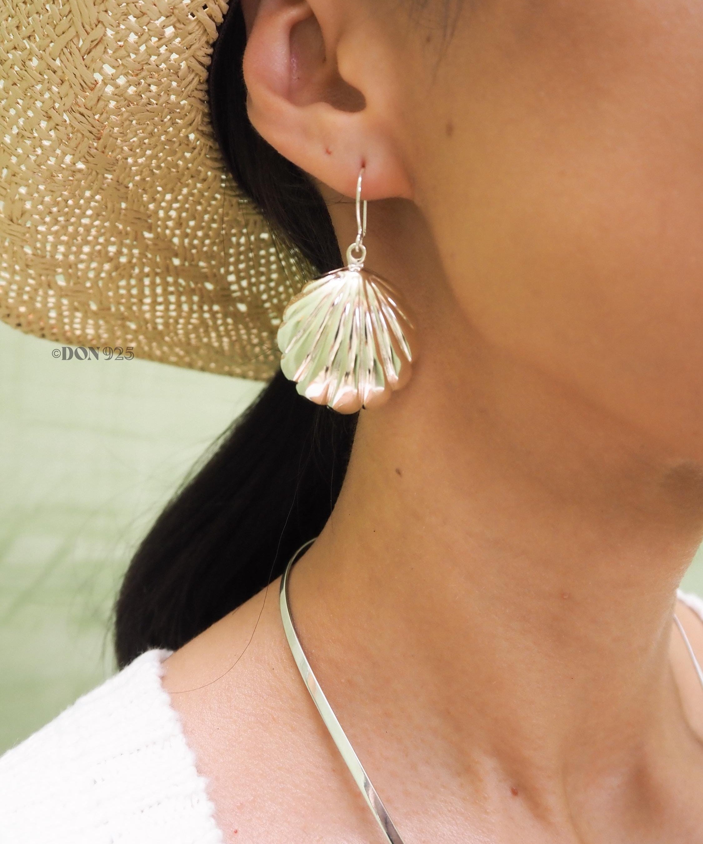 Big sterling silver seashell earring hanging from an ear.