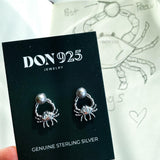 A pair of sterling silver earrings in the shape of a crab, holding a gray pearl