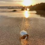 May include: A silver hammered ring on a sandy beach with the sun setting in the background.