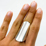 May include: A silver, wide, flat band ring worn on the middle finger of a hand with white nail polish.