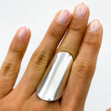 May include: A silver, wide, flat band ring worn on the middle finger of a hand with white nail polish.