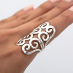 May include: A silver ring with a swirling, openwork design. The ring is wide and sits high on the finger.