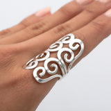 May include: A silver ring with a swirling, openwork design. The ring is wide and sits high on the finger.