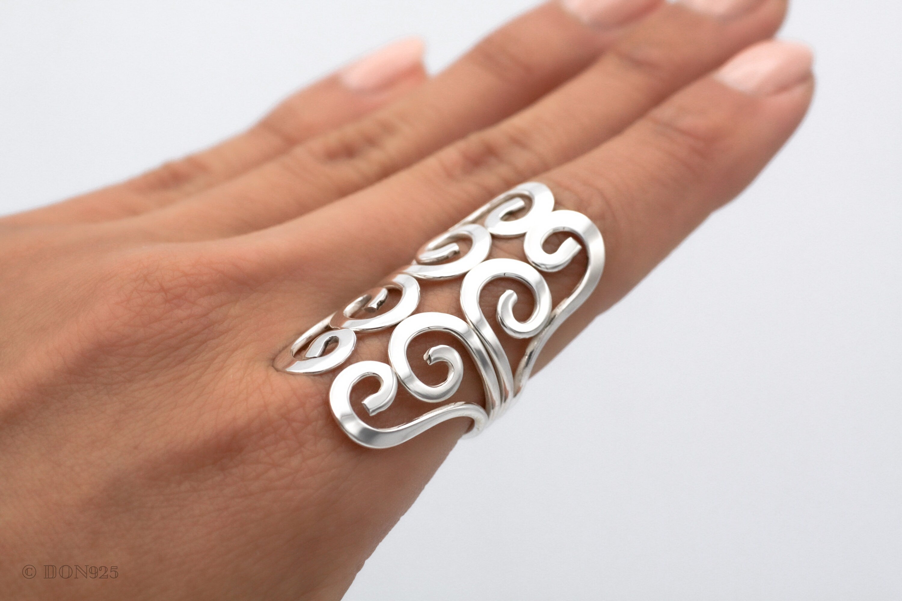 May include: A silver ring with a swirling, openwork design. The ring is wide and sits high on the finger.