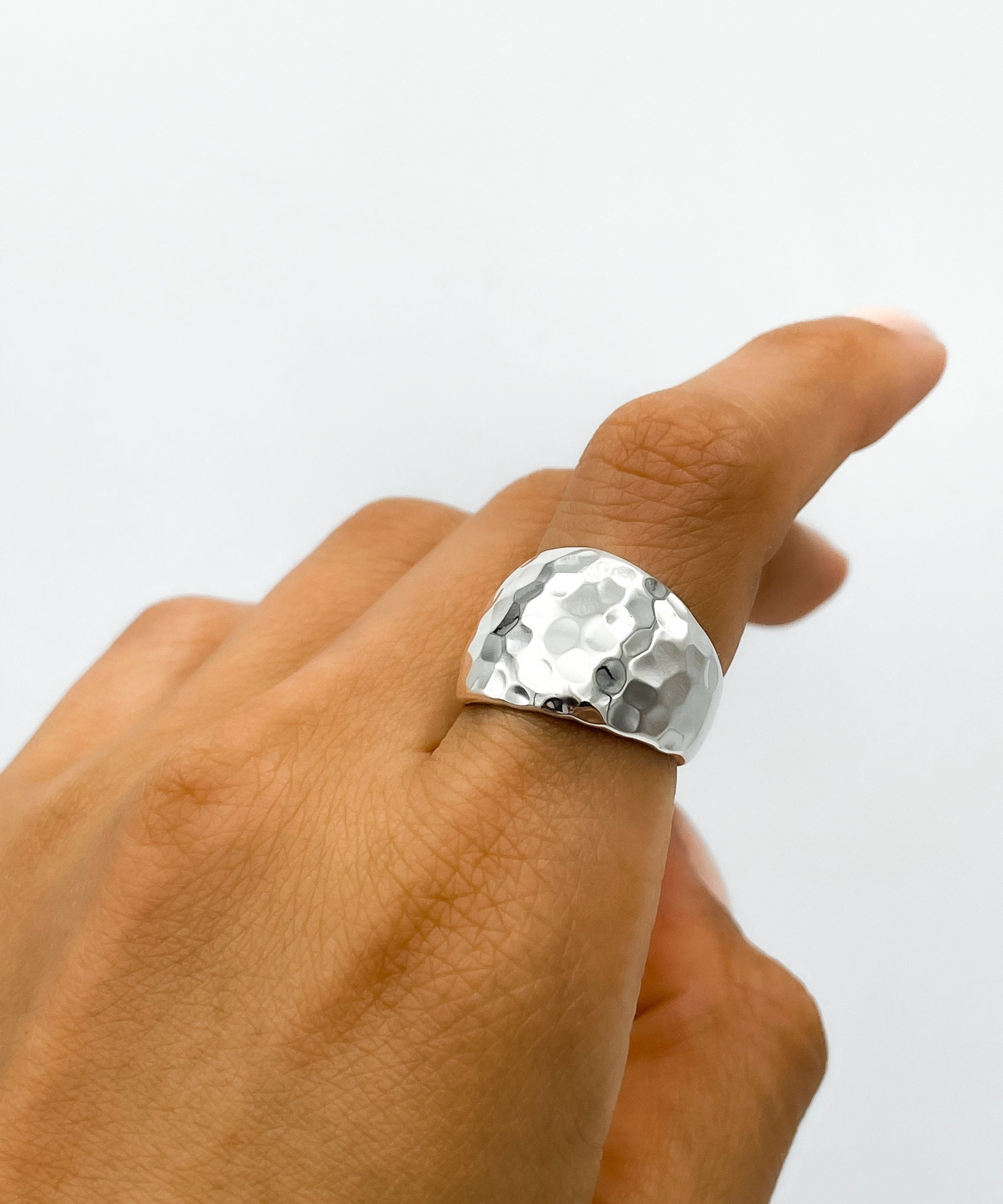 May include: A silver hammered ring with a wide band. The ring is worn on a person's finger.