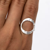 May include: A silver ring with a hammered, circular design. The ring is worn on a finger.