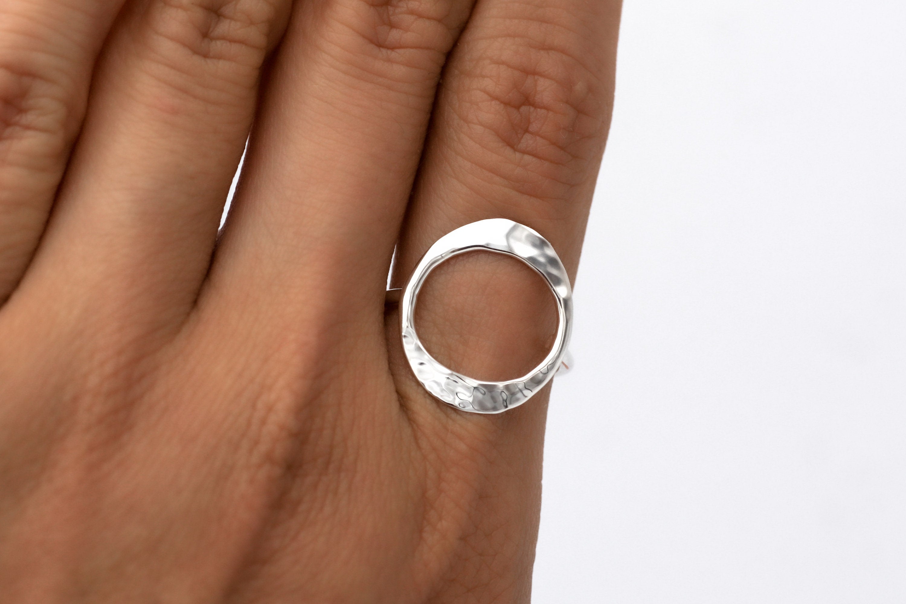 May include: A silver ring with a hammered, circular design. The ring is worn on a finger.