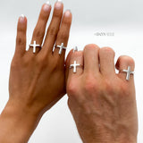 May include: Two hands wearing silver cross rings. The rings are simple and minimalist in design.