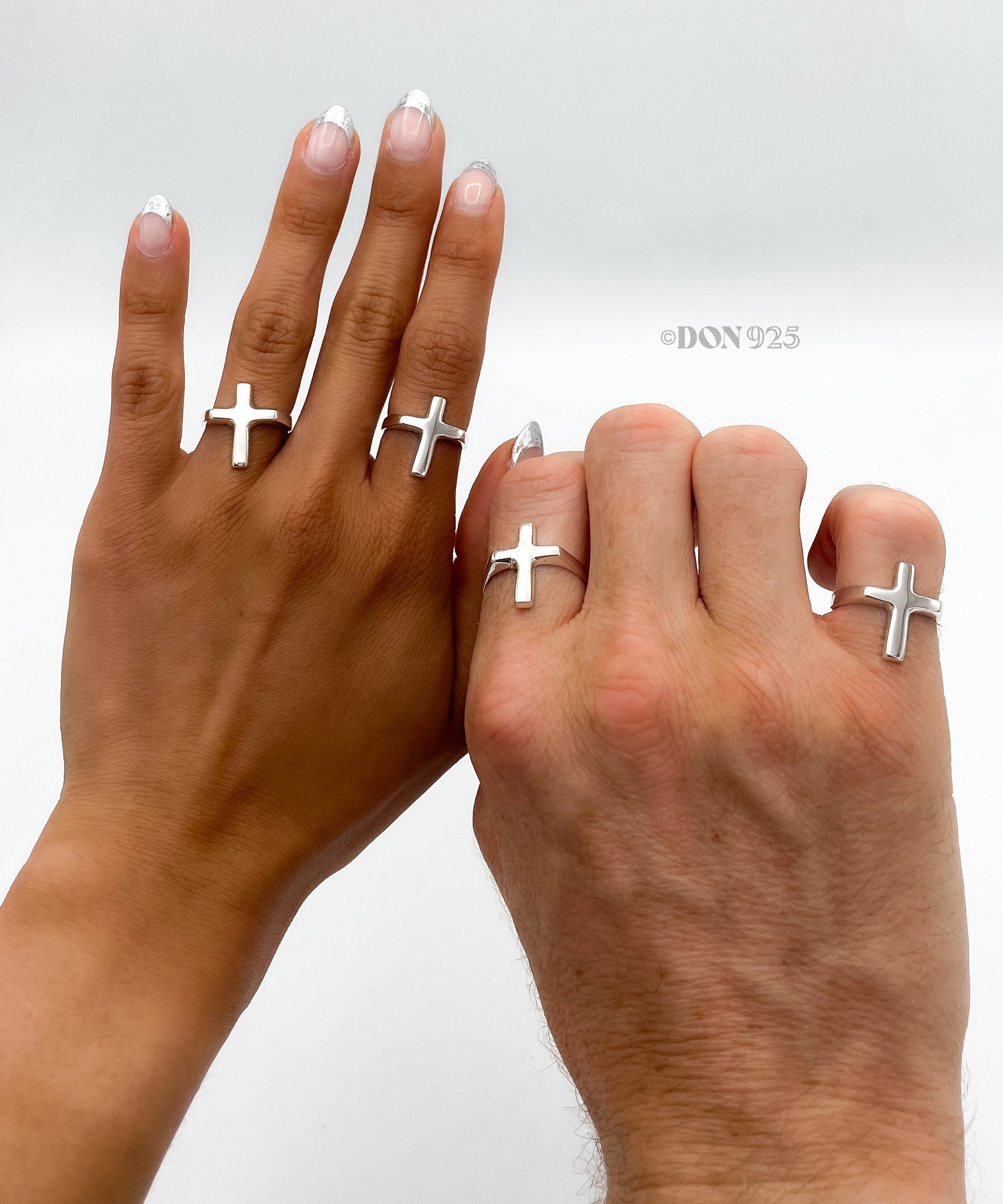 May include: Two hands wearing silver cross rings. The rings are simple and minimalist in design.