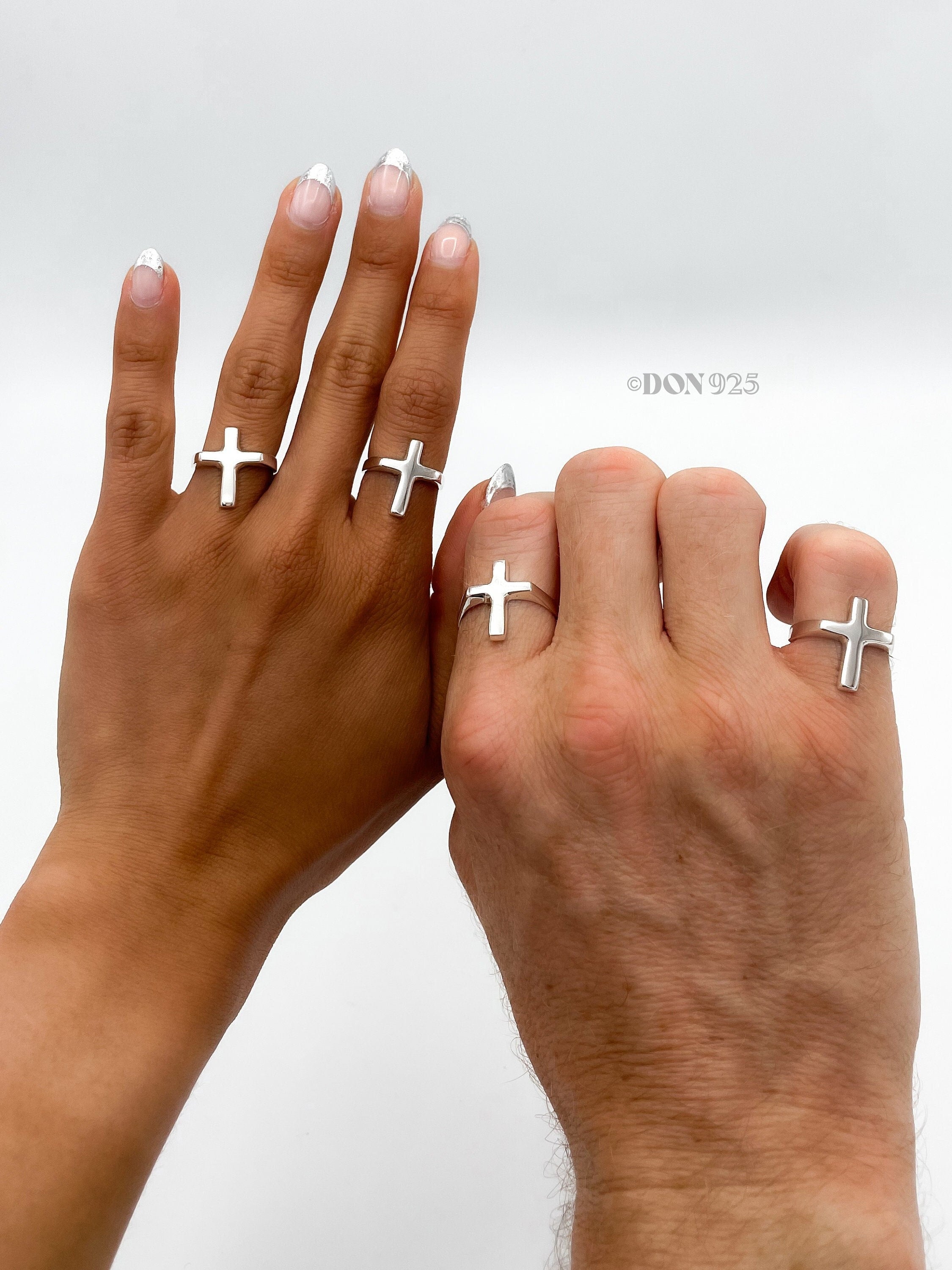 May include: Two hands wearing silver cross rings. The rings are simple and minimalist in design.