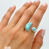 May include: A silver ring with two turquoise stones. The larger stone is a crescent shape and the smaller stone is round. The ring is on a person's finger.