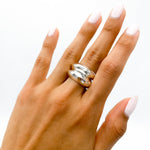 May include: A silver ring with a hammered texture. The ring is worn on the middle finger of a hand with light pink nail polish.