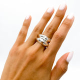 May include: A silver ring with a hammered texture. The ring is worn on the middle finger of a hand with light pink nail polish.