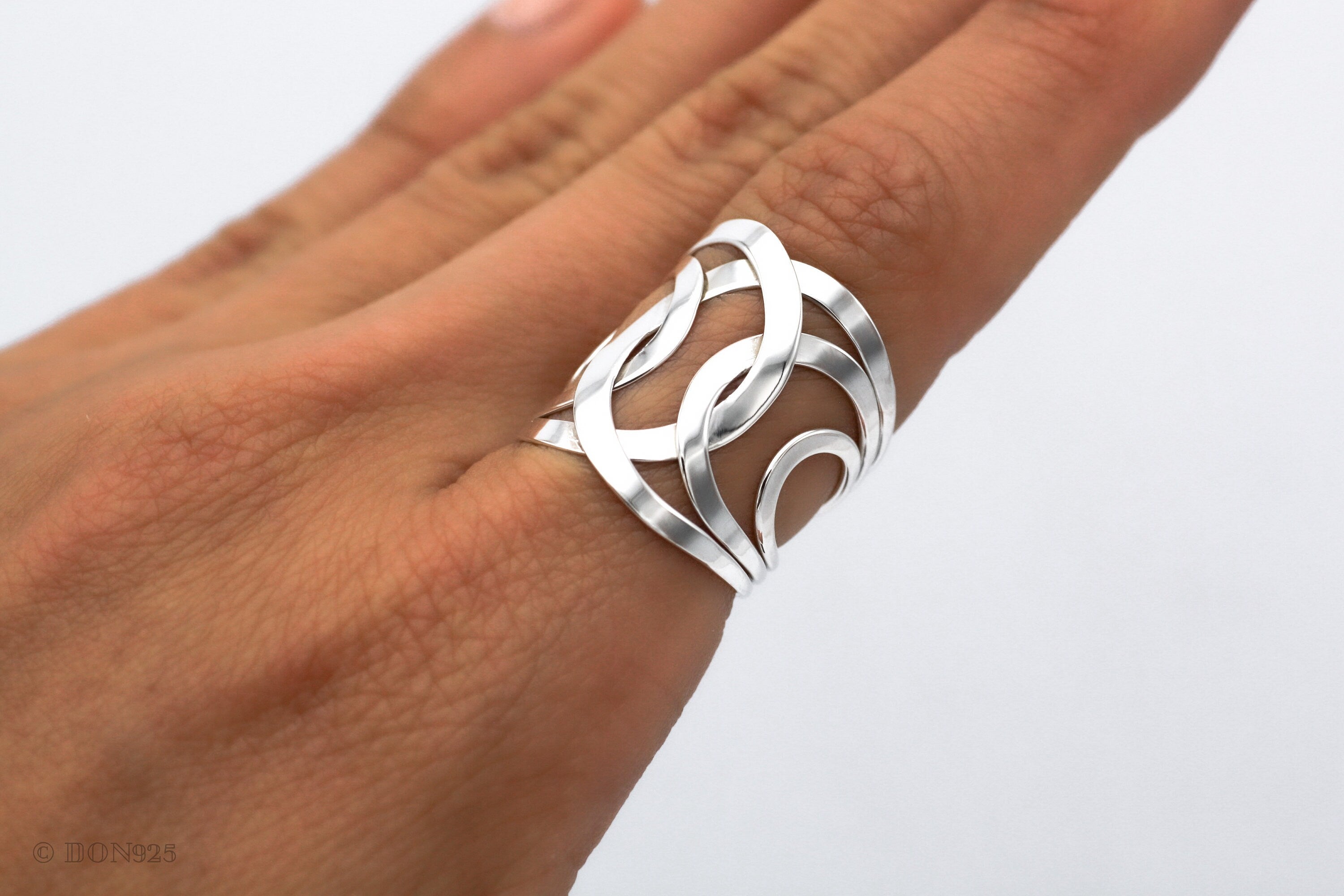 May include: A silver ring with a wide band featuring a geometric design of overlapping circles and curves.