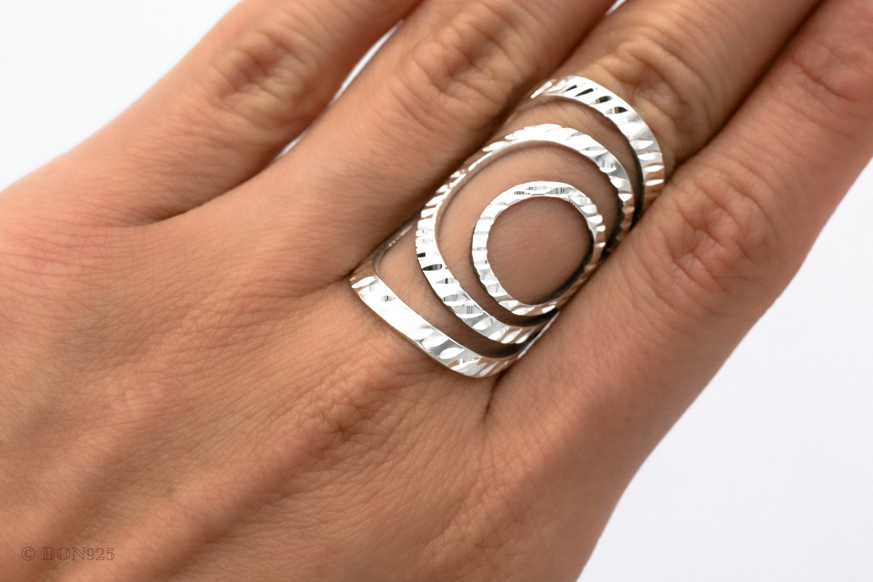 May include: A silver ring with a geometric design of overlapping circles. The ring is textured and has a modern, minimalist style.