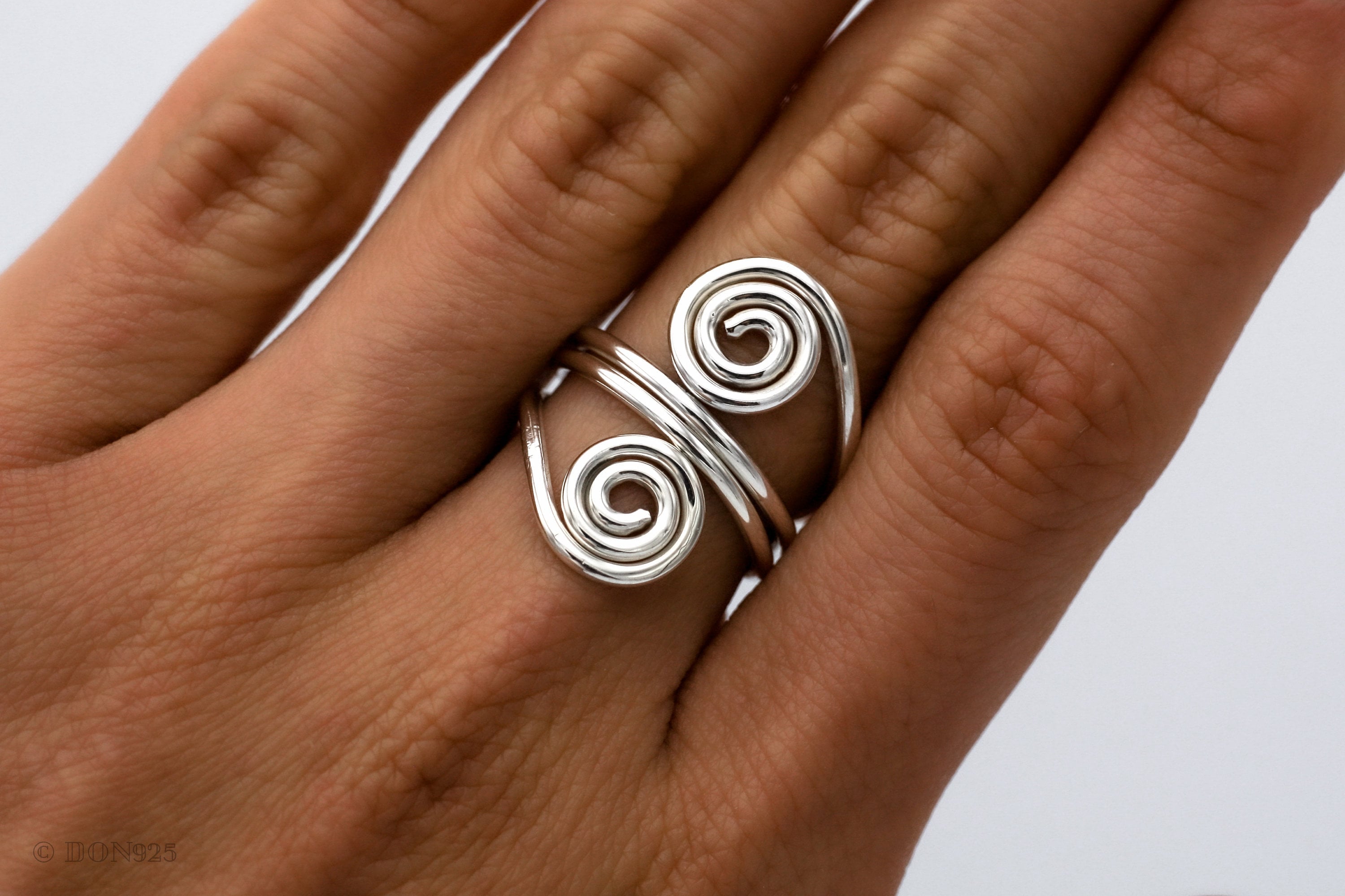 May include: A silver ring with two spiral designs. The ring is worn on a person's finger.