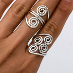 May include: Two silver rings with a spiral design. The ring on the index finger has two spirals, and the ring on the middle finger has four spirals.