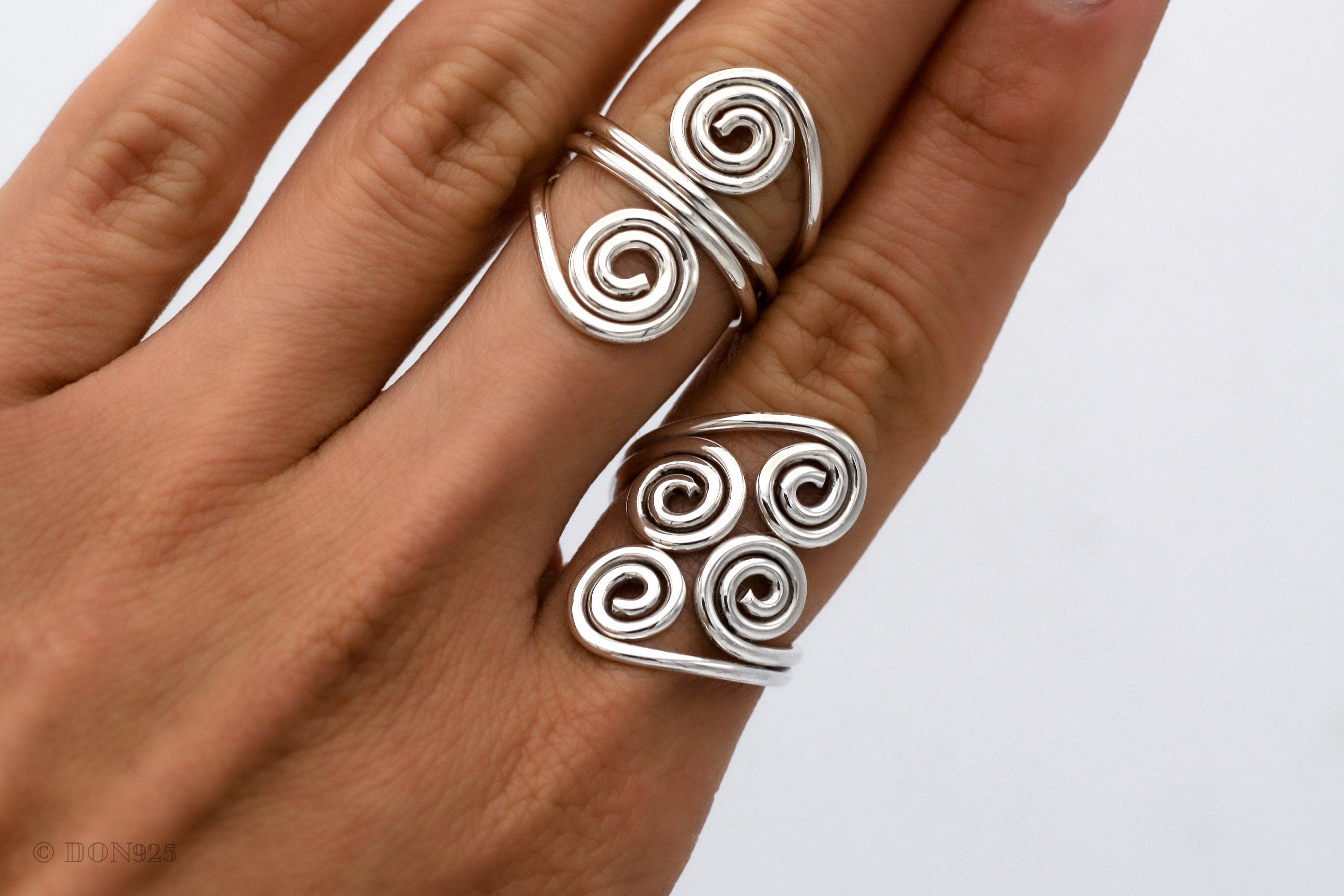 May include: Two silver rings with a spiral design. The ring on the index finger has two spirals, and the ring on the middle finger has four spirals.