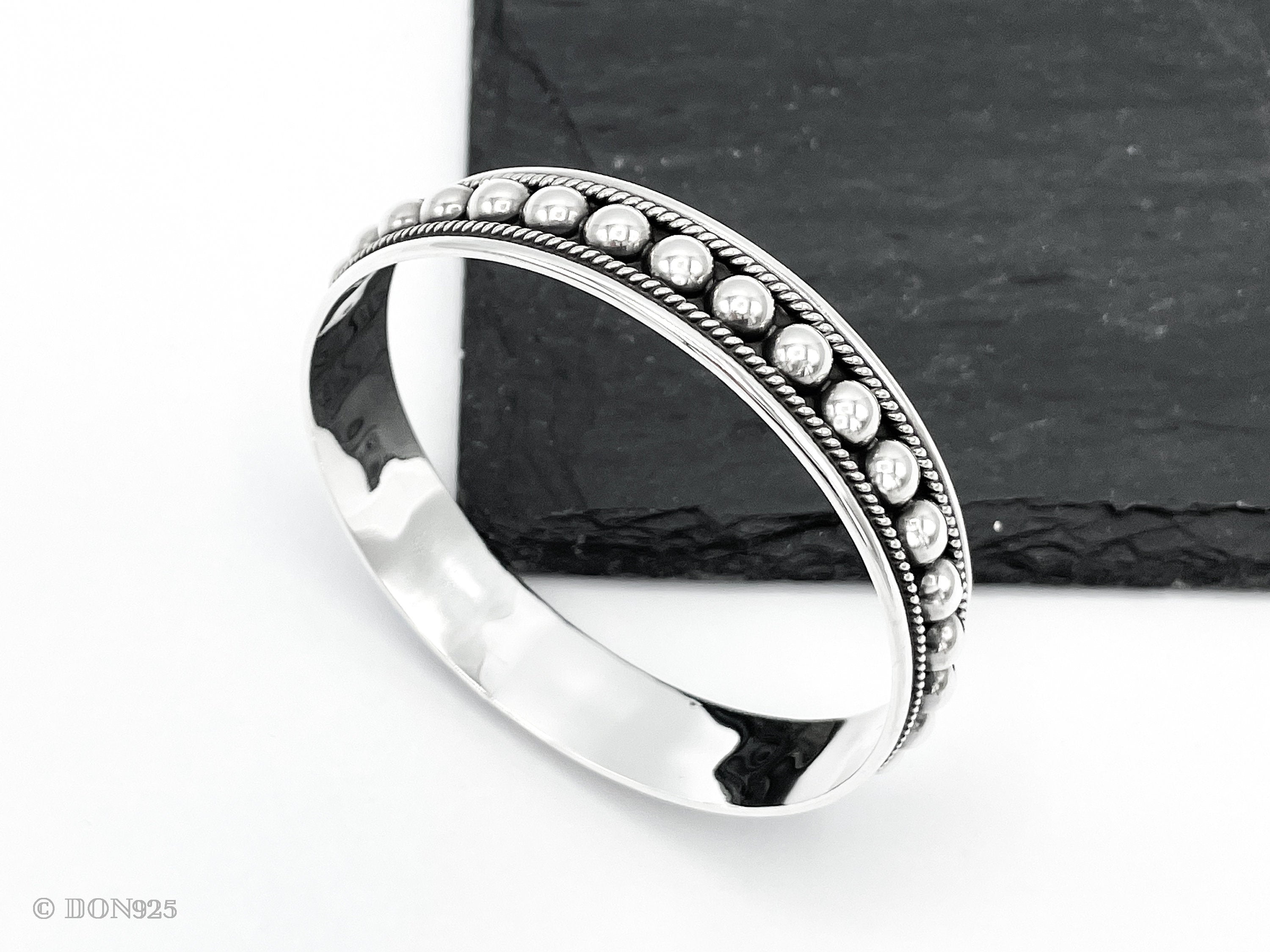 May include: A silver bangle bracelet with a beaded design. The beads are evenly spaced around the bracelet and are slightly raised from the surface.