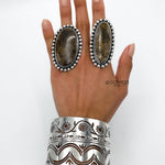 May include: Two silver rings with brown stone inlays and a silver cuff bracelet with a floral design.