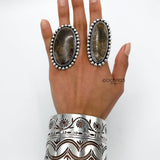 May include: Two silver rings with brown stone inlays and a silver cuff bracelet with a floral design.