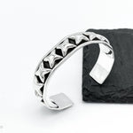 May include: A silver cuff bracelet with a row of raised star-shaped details. The bracelet is open and has a smooth, rounded finish.