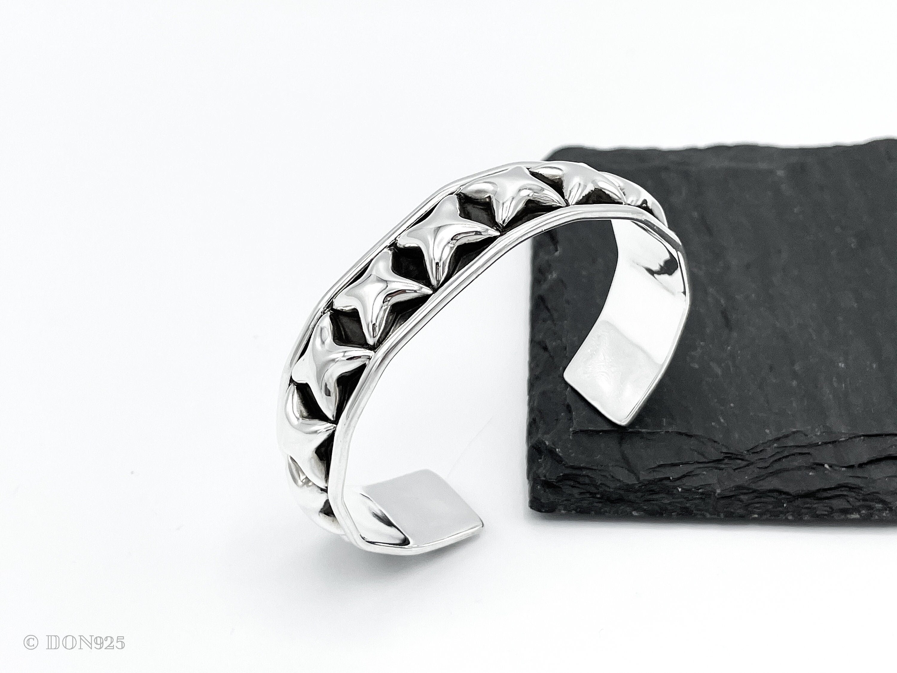 May include: A silver cuff bracelet with a row of raised star-shaped details. The bracelet is open and has a smooth, rounded finish.