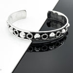 May include: A silver bangle bracelet with a decorative band of circles and raised dots.