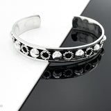 May include: A silver bangle bracelet with a decorative band of circles and raised dots.