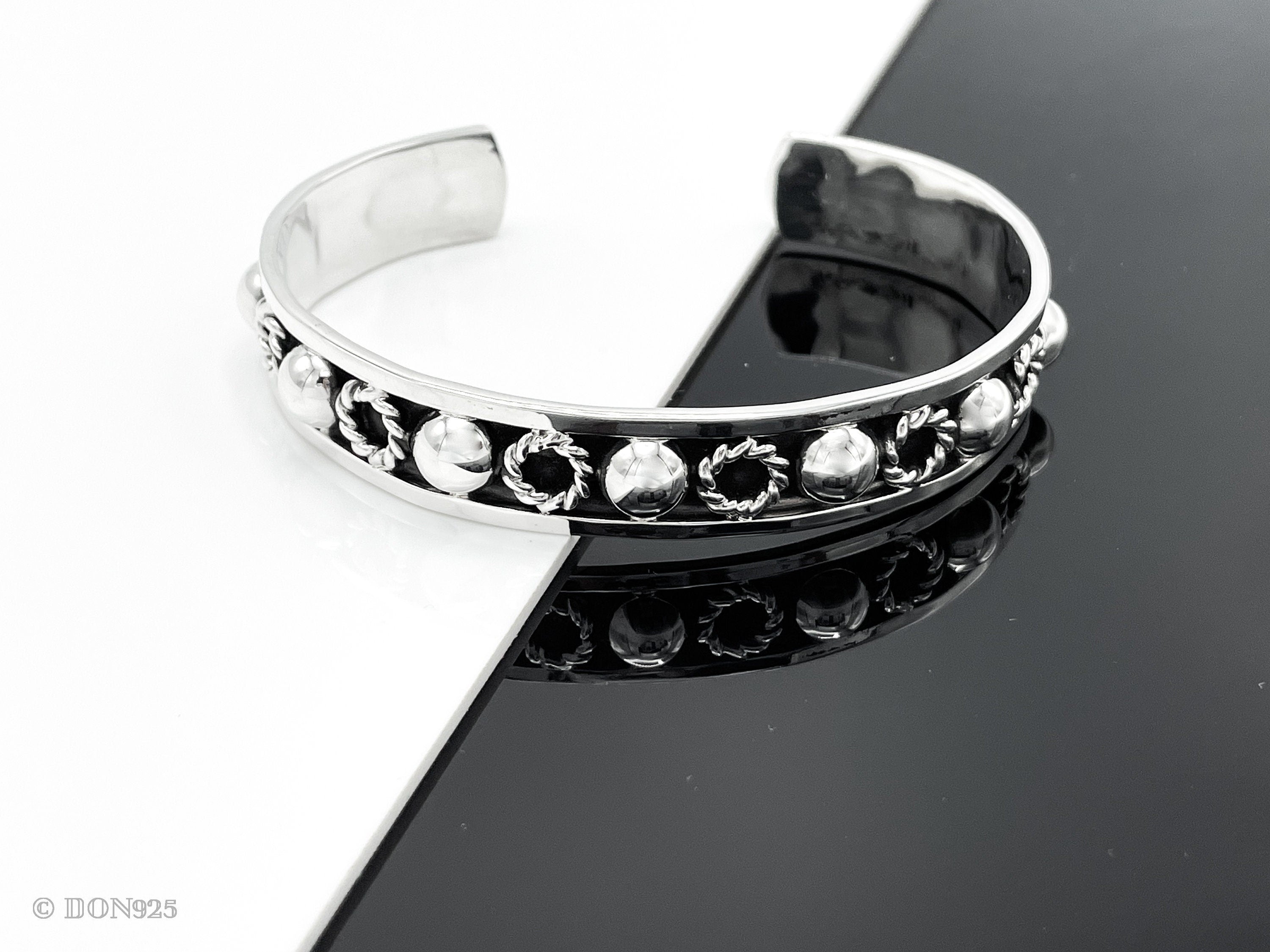 May include: A silver bangle bracelet with a decorative band of circles and raised dots.
