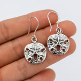 May include: Silver dangle earrings featuring a textured, round sand dollar design with a starfish in the center.